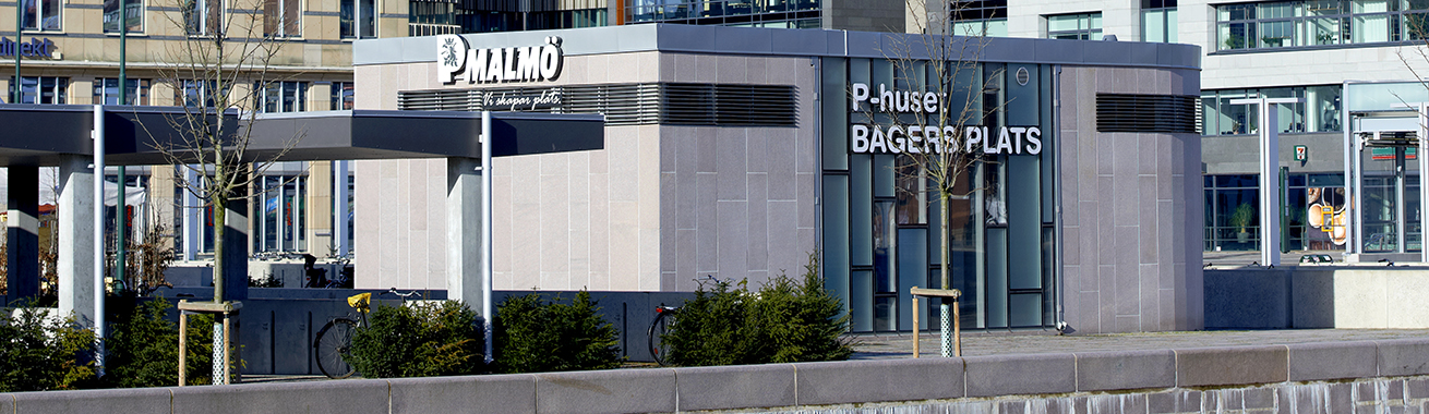 Gångentré till P-huset Bagers plats med logotype i vitt. Cykelställ i förgrunden och olika byggnader i bakgrunden